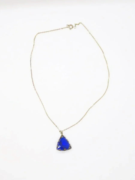 This extraordinary Art Deco pendant necklace is a true collector's treasure, featuring a stunning triangular faceted cobalt blue glass stone that shifts between rich cobalt and mesmerizing violet tones depending on the light.