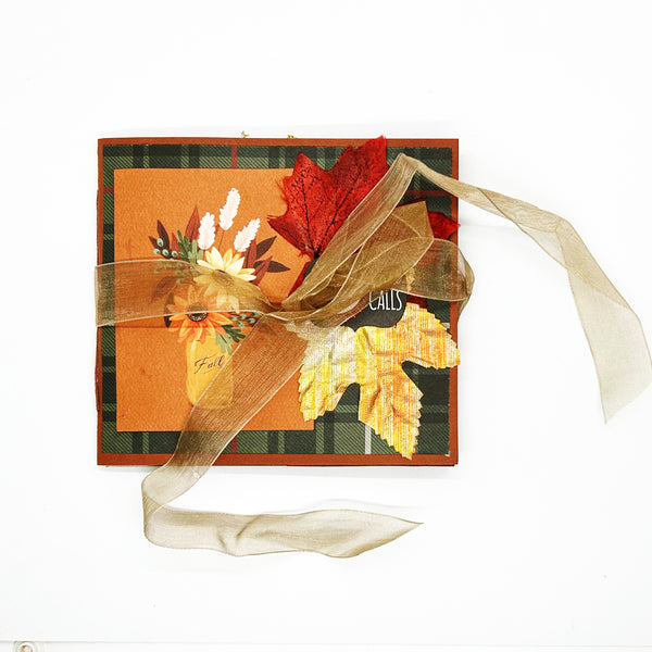 Handmade autumn mini scrapbook album featuring a green and brown plaid pattern, orange paper cover, decorative fall leaves, and a large golden ribbon bow