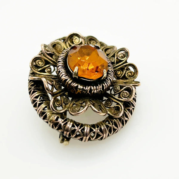 This lovely vintage brooch has a beautiful golden faceted oval stone surrounded by layers of elaborately detailed filigree. The workmanship is outstanding. The stone is prong set and secure; it's a very wearable brooch. It measures 1.5" across and is in very good condition.