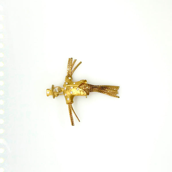 Detailed close-up of a vintage figural scarecrow brooch showing the textured metal patterns, embedded clear chaton rhinestones, and individual strands of fluid herringbone chain hanging from the tors