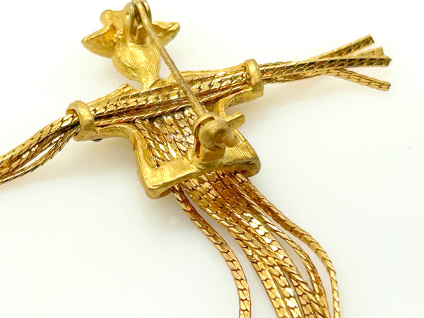 Detailed close-up of a vintage figural scarecrow brooch showing the textured metal patterns, embedded clear chaton rhinestones, and individual strands of fluid herringbone chain hanging from the tors