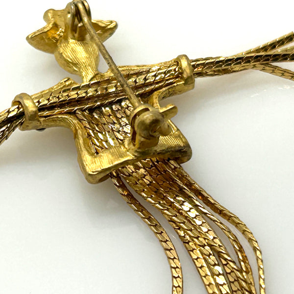 Detailed close-up of a vintage figural scarecrow brooch showing the textured metal patterns, embedded clear chaton rhinestones, and individual strands of fluid herringbone chain hanging from the tors