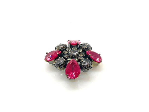 Vintage costume jewelry brooch pin featuring a central rhinestone cluster encircled by a halo of clear crystals, with alternating pear-cut pink faux rubies and round faceted gunmetal black stones in a dark metallic prong setting.