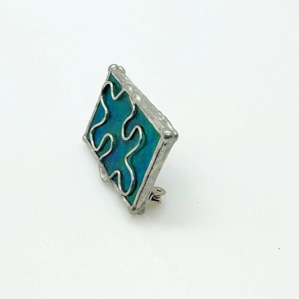 This charming stained glass pin celebrates individuality with a puzzle piece design crafted using authentic Tiffany-style copper foil work. Vibrant green and blue glass pieces are carefully soldered together to create a wearable conversation starter that doubles as meaningful advocacy.