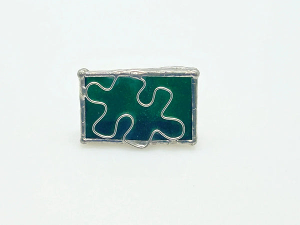 This charming stained glass pin celebrates individuality with a puzzle piece design crafted using authentic Tiffany-style copper foil work. Vibrant green and blue glass pieces are carefully soldered together to create a wearable conversation starter that doubles as meaningful advocacy.