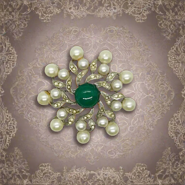 Measuring 1 3/4" wide, the brooch features a striking green round cabochon centerpiece surrounded by elegant swirling patterns. Cream faux pearls add a soft, classic touch, all set in a lustrous silver-tone metal that enhances its vintage appeal