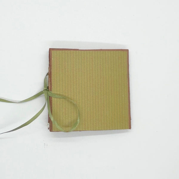 Handmade mini autumn scrapbook album with an orange and green striped patterned cover, featuring a cartoon fox illustration, a die-cut red maple leaf, a gold heart, and the text "HELLO FRIEND." A green satin ribbon closure extends from the side of the book, which sits on a wooden shelf against a brick background.

