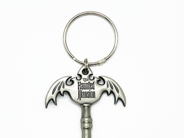 Key-shaped keychain with bat design and 'The Haunted Mansion' logo on a white background