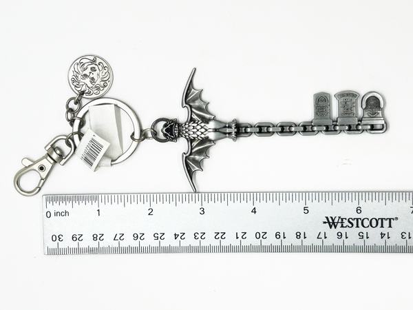 Metal keychain with decorative elements on a white background with a ruler for scale.
