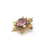 A gold-toned brooch with a central heart-shaped, light purple gemstone. The brooch is surrounded by ornate gold filigree, small pearls, and clear crystals, creating a vintage, elegant design.