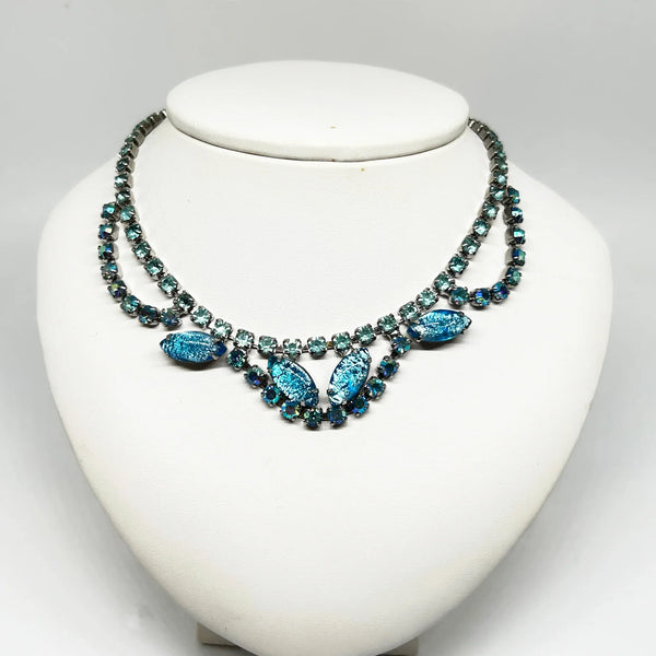 This exquisite brooch with an Old World aesthetic showcases finely crafted gold filigree petals encircling a square stone in elegant blue-purple tones. Between each delicate petal rests a round, iridescent stone that complements the central hues, adding subtle depth and shimmer.