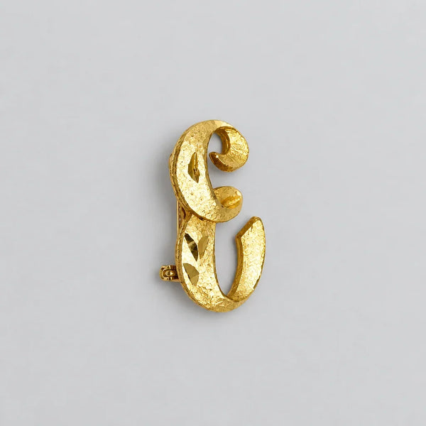 A small, vintage gold-tone initial "E" cursive monogram brooch pin, featuring a dual-textured finish with brushed matte styling and diamond-cut highlights on a plain white background