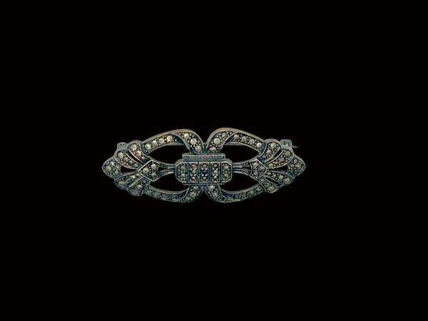 Vintage Art Deco sterling silver bar brooch featuring an openwork geometric design inlaid with shimmering marcasite stones, isolated on a black background.