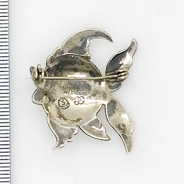 This is a whimsical brooch in the shape of a fish. The detailing on the scales and fins is particularly nice. It measures 1.25” across. Add a touch of charm to any outfit with our Vintage Mexican Silver Fish Brooch. You'll love the intricate detailing on the scales and fins, giving it a unique and whimsical touch. At 1.25" across, it's the perfect size for everyday wear.