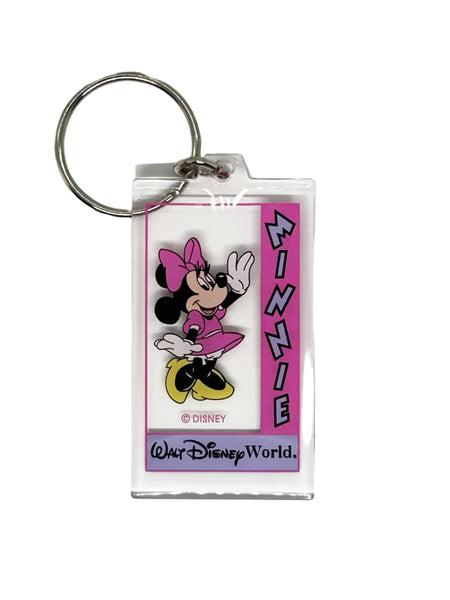 This Minnie Mouse keychain is too cute. It is made of clear acrylic, and shows Minnie Mouse in a pink dress, a pink bow, white gloves and yellow shoes. She has a big smile and is waving. The letters on the left side read "Minnie" in lavender with black border, on a bright pink background. Below Minnie is a purple banner with "Walt Disney World" in black