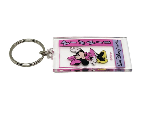 This Minnie Mouse keychain is too cute. It is made of clear acrylic, and shows Minnie Mouse in a pink dress, a pink bow, white gloves and yellow shoes. She has a big smile and is waving. The letters on the left side read "Minnie" in lavender with black border, on a bright pink background. Below Minnie is a purple banner with "Walt Disney World" in black