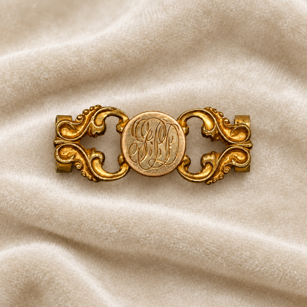 Antique Victorian monogrammed watch slide in gold-tone metal. Features a round hand-engraved monogram center and highly detailed repoussé scrollwork side accents, perfect as a jewelry making component