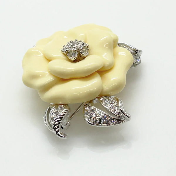 Vintage Nolan Miller Lara camellia flower brooch featuring carved cream lucite petals, a central clear rhinestone cluster, and textured silver-tone metal leaves