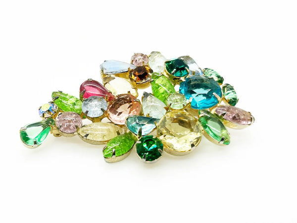 This gorgeous vintage brooch features a multicolored array of stones, including aqua, pale gold, shades of green, pink, and blue in round, marquise, and pear shapes.