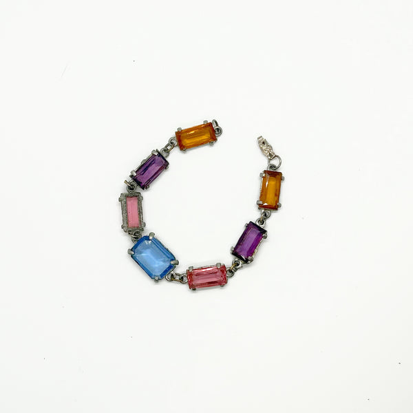 A silver-tone chain bracelet featuring rectangular gemstones in orange, purple, pink, and light blue, arranged in an oval shape on a plain white background.