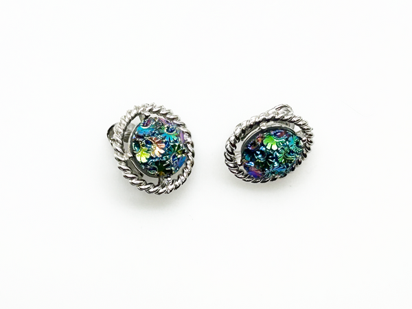 Discover the captivating allure of these authentic Sarah Coventry "Northern Lights" clip-on earrings, a stunning find from the 1960s-70s era. The dichroic glass centers showcase an extraordinary color-shifting quality that transforms from blue to green to purple to red as light dances across the surface—creating a mesmerizing effect that draws admiration from every angle.