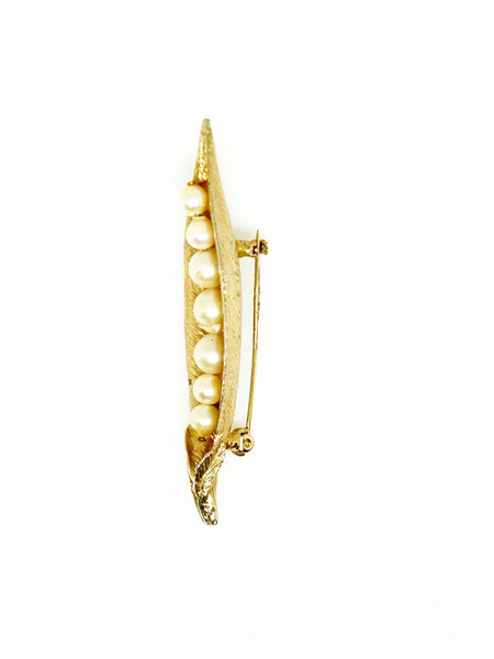 This vintage-inspired brooch features a brushed gold finish and showcases seven delicately graduated faux pearls, measuring 2.75 inches in length.
