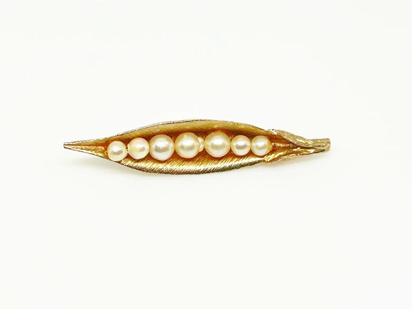 This vintage-inspired brooch features a brushed gold finish and showcases seven delicately graduated faux pearls, measuring 2.75 inches in length.