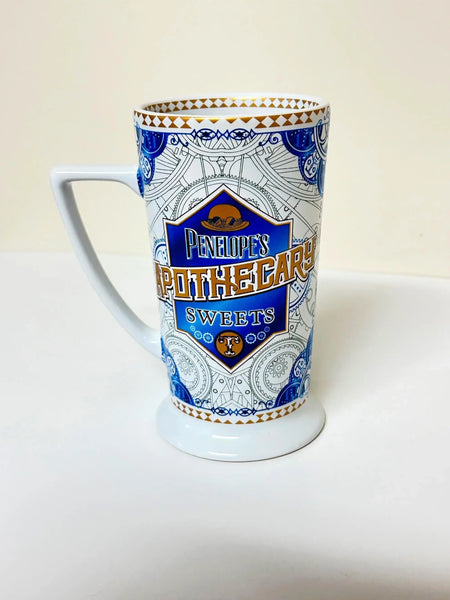 Universal Studios Toothsome Chocolate Emporium Penelope's Apothecary Sweets tall ceramic pedestal mug with blue, white, and gold geometric pattern on a solid white background.
