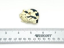 A vintage DKI gold-tone enamel brooch shaped like two snuggling black and white spotted pigs on a white background.