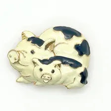 A vintage DKI gold-tone enamel brooch shaped like two snuggling black and white spotted pigs on a white background.