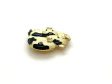 A vintage DKI gold-tone enamel brooch shaped like two snuggling black and white spotted pigs on a white background.
