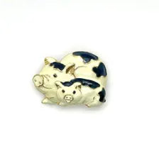 A small pig-shaped brooch or charm with a cream-colored body and black patches, photographed on a plain white background.
