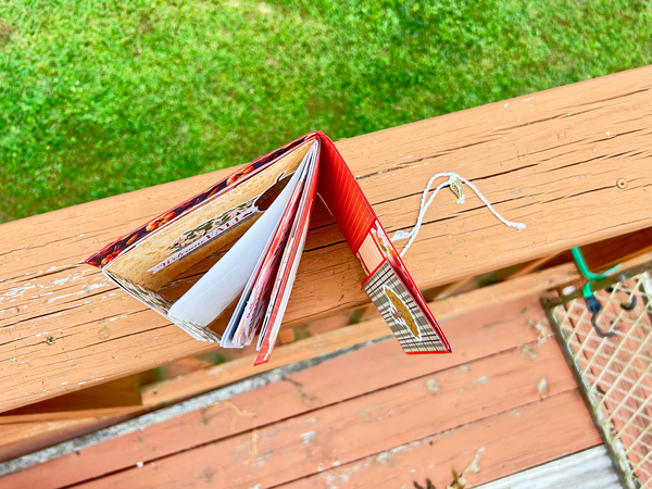 Handmade autumn mini scrapbook album with a rustic brown wood-plank pattern cover, wrapped with a bright orange paper band. The cover features a dark shield-shaped tag with an illustration of a "Fall Latte" whipped cream drink and red text that reads "Pumpkin Spice."