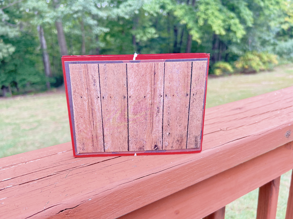 Handmade autumn mini scrapbook album with a rustic brown wood-plank pattern cover, wrapped with a bright orange paper band. The cover features a dark shield-shaped tag with an illustration of a "Fall Latte" whipped cream drink and red text that reads "Pumpkin Spice."