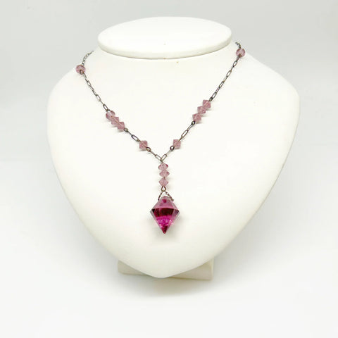 This stunning vintage crystal necklace showcases clusters of deep purple bicone beads, interspersed with sleek paper clip chains. It culminates in a magnificent faceted diamond-shaped stone. Measuring 16.5 inches in length, with a drop of 1.5 inches from the center, this piece exudes elegance and sophistication.
