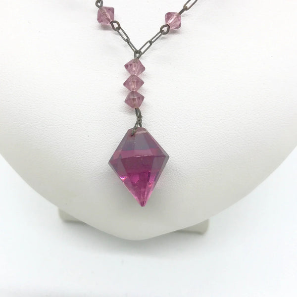 This stunning vintage crystal necklace showcases clusters of deep purple bicone beads, interspersed with sleek paper clip chains. It culminates in a magnificent faceted diamond-shaped stone. Measuring 16.5 inches in length, with a drop of 1.5 inches from the center, this piece exudes elegance and sophistication.