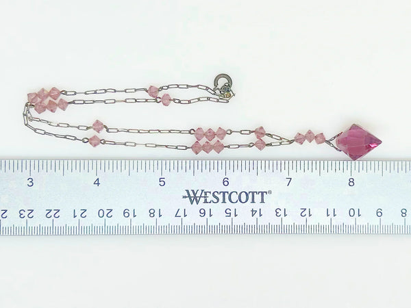 This stunning vintage crystal necklace showcases clusters of deep purple bicone beads, interspersed with sleek paper clip chains. It culminates in a magnificent faceted diamond-shaped stone. Measuring 16.5 inches in length, with a drop of 1.5 inches from the center, this piece exudes elegance and sophistication.