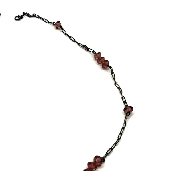 A vintage necklace featuring clusters of deep purple bicone crystal beads on a dark-toned paperclip chain, culminating in a large, heavily faceted diamond-shaped purple crystal drop pendant