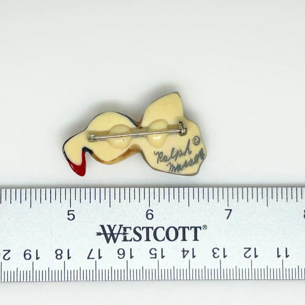 This is a brooch by artist Ralph Massey, who is acclaimed for many types of artwork- acrylic, performance, resin and more. This brooch is resin, hand made and hand painted in white, black, red-orange and gray. It depicts a penguin standing on rock, and measures about 1.75” inches tall.