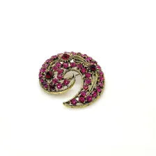 Close-up detail of a mid-century paisley swirl pin showing the openwork metal vines and prong-set pink and red rhinestone crystals