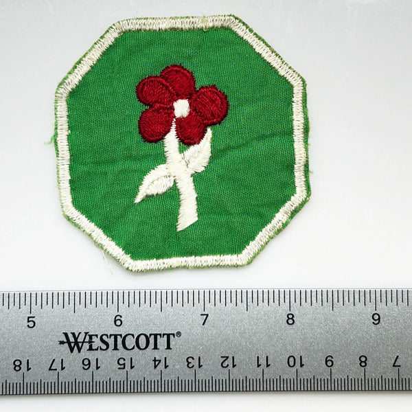 This is a vintage Girl Scout troop crest patch, featuring a red flower design with a white center and stem on a green octagonal background. This specific design has been retired. It depicts either a Scarlet Pimpernel or a Cardinal Flower, with the specific name depending on the era 