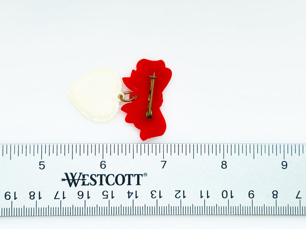 This lovely and nostalgic piece is a vintage early plastic sweetheart bow with dangling filigree lace heart brooch pin, often described as a "Heart Within a Heart" design. It is a recognized "book piece" in vintage jewelry collecting and was commonly made from materials like celluloid plastic .