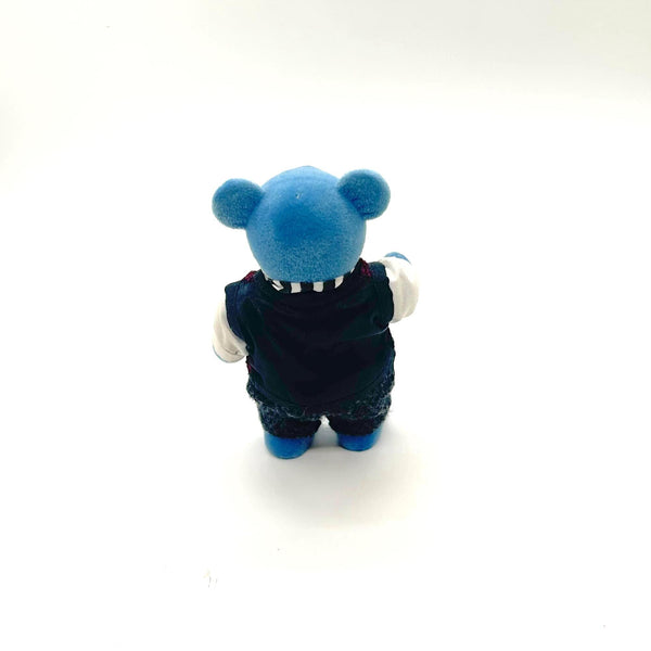 A small blue plush toy figure shown from the back, wearing a dark navy outfit with white gloves and blue shoes, photographed on a plain white background.