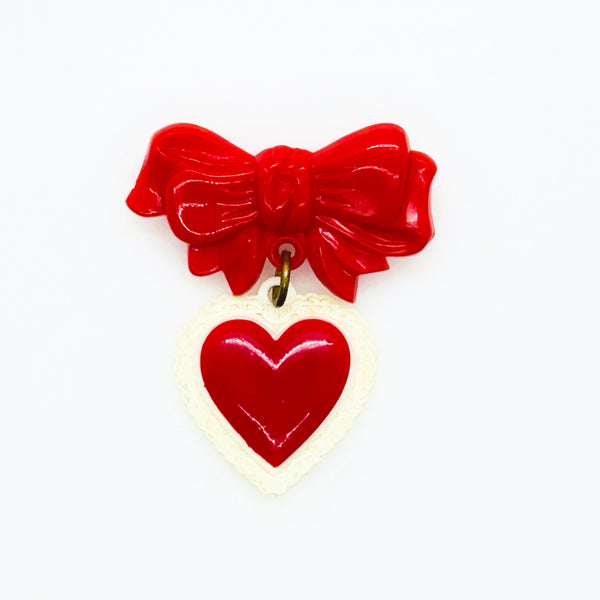 This lovely and nostalgic piece is a vintage early plastic sweetheart bow with dangling filigree lace heart brooch pin, often described as a "Heart Within a Heart" design. It is a recognized "book piece" in vintage jewelry collecting and was commonly made from materials like celluloid plastic .