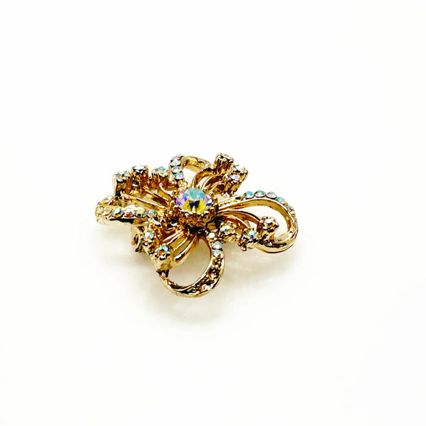 This is a three dimensional vintage ribbon brooch featuring clear rhinestones and a central aurora borealis (AB) gemstone, designed in an abstract floral or bow shape. 