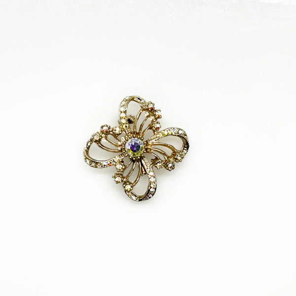 This is a three dimensional vintage ribbon brooch featuring clear rhinestones and a central aurora borealis (AB) gemstone, designed in an abstract floral or bow shape. 