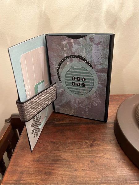 Celebrate determination and achievement with the She Believed Mini Album, a beautifully handcrafted journal that inspires and motivates. This carefully designed keepsake features intricate details, multiple slots, and inserts to hold cherished memories, including two additional mini journals tucked inside