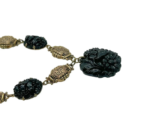 An Art Deco choker necklace with gold-tone filigree links and three dark, intricately carved floral beads, featuring a larger central pendant drop