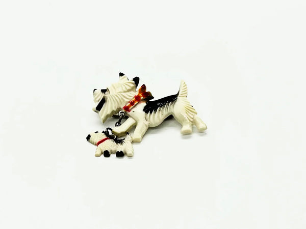 This is such an adorable pin. It is made of two black and white terrier dogs, one larger and the other smaller, puppy. The larger dog measure 1.25” across and wears a red, orange and white checked collar; the puppy wears a solid red collar and measures 1/2” across. 