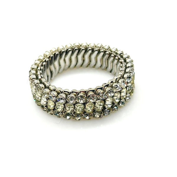 A close-up studio shot of a vintage silver-tone rhinestone expansion bracelet, featuring three rows of prong-set clear gemstones on a flexible, metallic accordion-style expansion band, shown against a plain white background